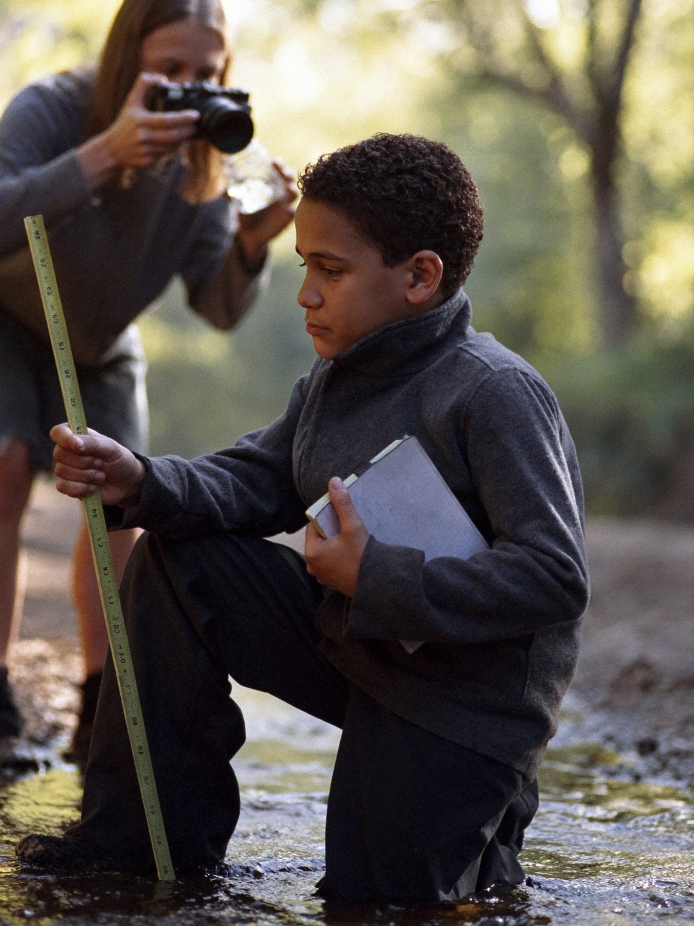 A boy measuring a creek bed while his sister photographs a water sample